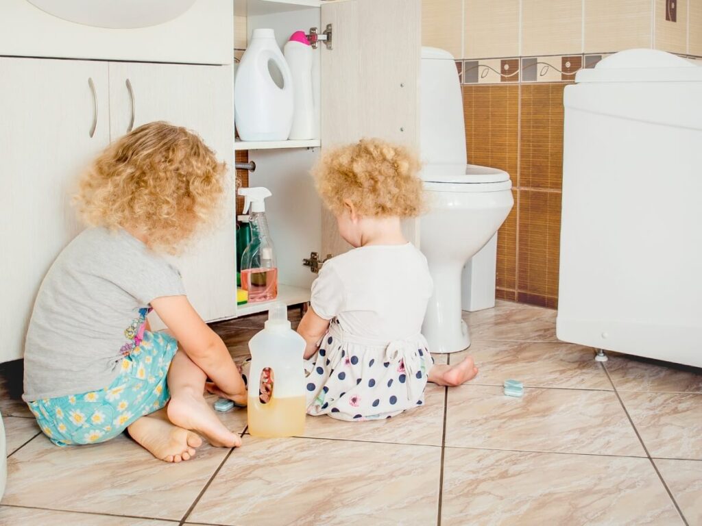 Dve deti vyťahujúce čistiace prostriedky z kúpeľňovej skrinky.